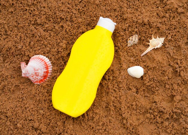 Botella amarilla de aceite de protección solar en la arena con conchas marinas Bronceado Protección de la piel en unas vacaciones en la playa co