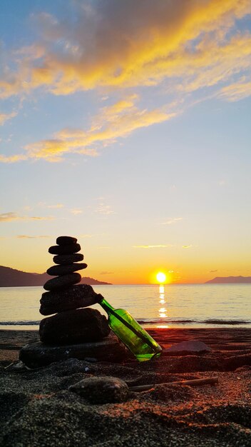 Foto botella apoyada en una pila de piedras en la playa contra el cielo durante la puesta de sol