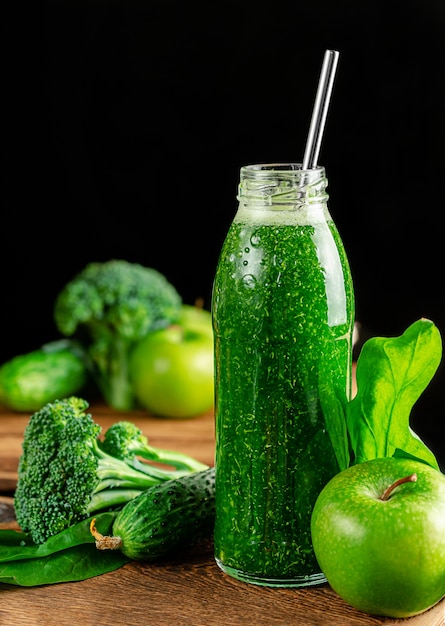 Botella de batido alcalino verde con ingredientes en la pared oscura.