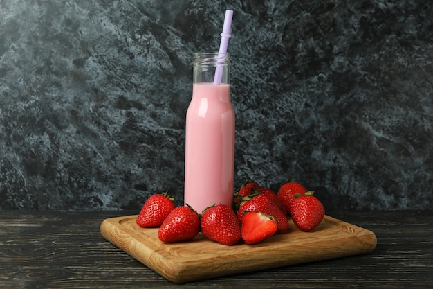 Botella de batido de fresa e ingredientes sobre mesa de madera