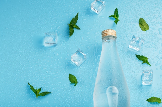 Botella con una bebida helada, cubitos de hielo, gotas y hojas de menta