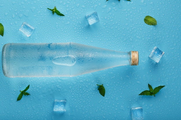 Botella con una bebida helada, cubitos de hielo, gotas y hojas de menta