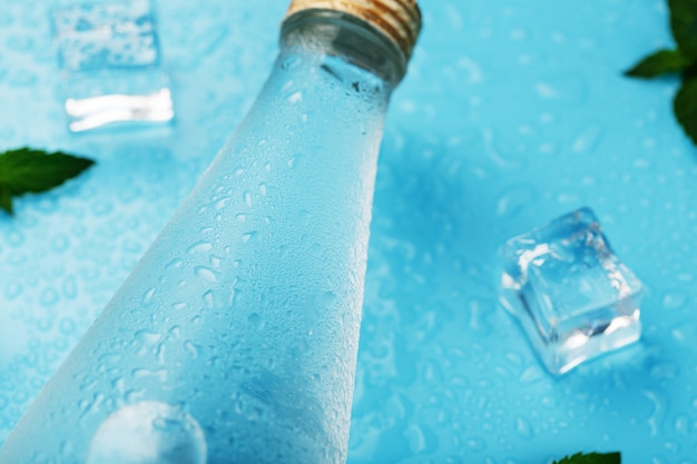 Botella con una bebida helada, cubitos de hielo, gotas y hojas de menta