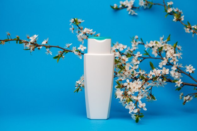 botella blanca con crema, champú para el cabello, gel de ducha, fondo azul aislado, belleza y juventud del cuerpo humano, árbol en flor