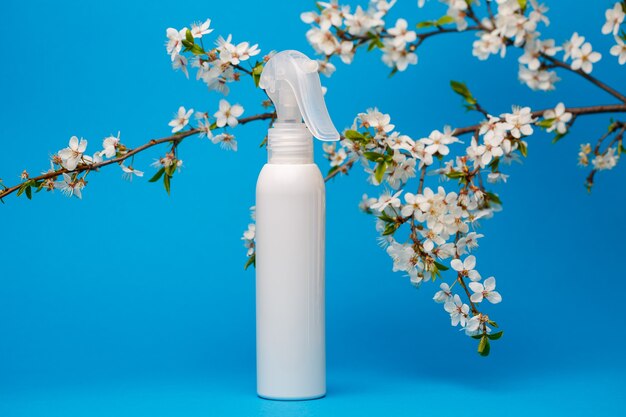 botella blanca con crema, champú para el cabello, gel de ducha, fondo azul aislado, belleza y juventud del cuerpo humano, árbol en flor