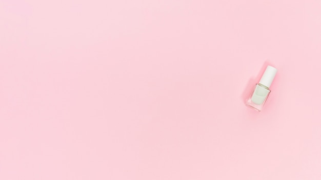 Foto botella blanca de esmalte de uñas en fondo rosado con espacio de copia para escribir el texto