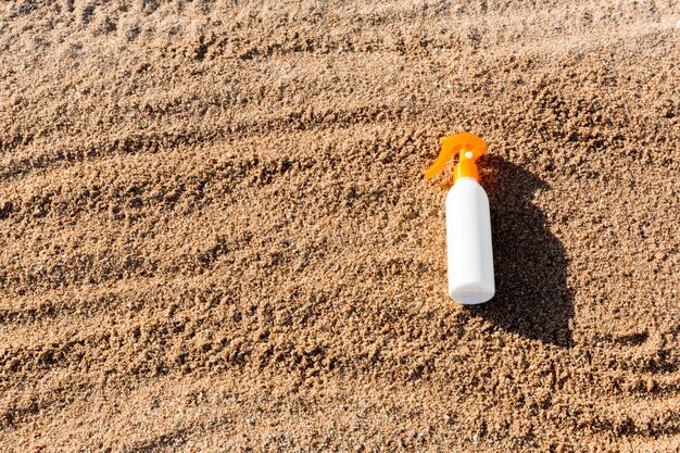 Botella blanca de la loción de bronceado en la arena con el espacio de la copia. crema de protección solar spf en la playa del mar en concepto de vacaciones de verano
