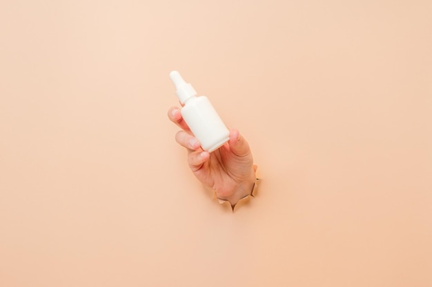 Foto botella blanca con loción sérica o aceite esencial ácido hialurónico y colágeno en la mano sobre fondo beige concepto de cosméticos para el cuidado de la piel volante de belleza