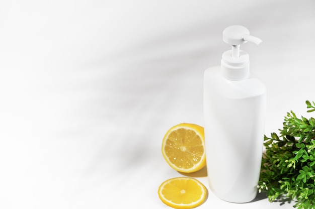 Botella blanca sin marca con limón y plantas verdes. Envase con dosificador de productos cosméticos naturales. Frasco en blanco para loción, crema, loción corporal, champú o acondicionador para el cabello. Estilo de maqueta.