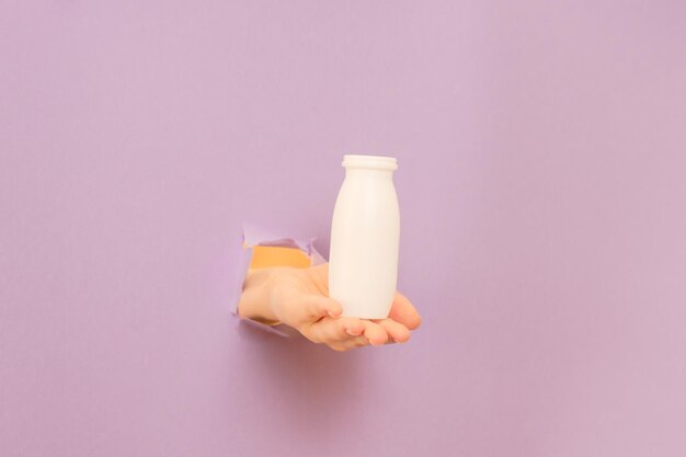 Botella blanca de yogur probiótico para el sistema digestivo en la mano con fondo lila suplementos dietéticos para el estómago