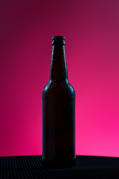 Foto botella de cerveza sin etiqueta sobre un fondo rosa