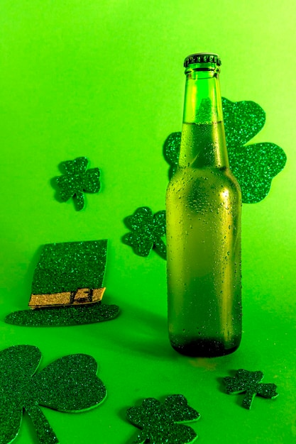 Foto botella de cerveza fría verde sobre fondo verde con trébol y sombrero, vertical del día de san patricio