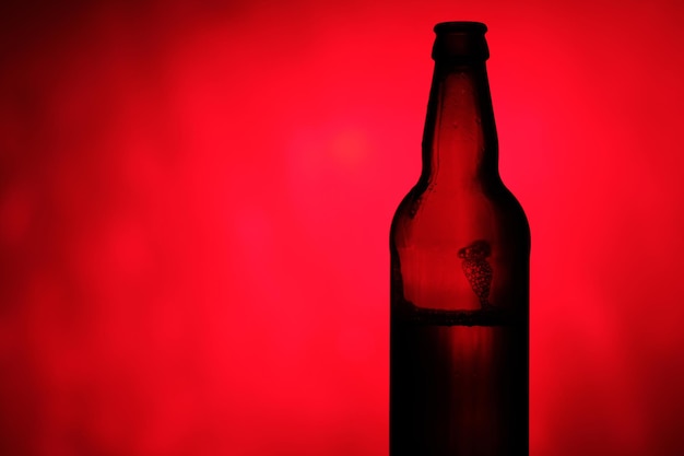 Foto botella de cerveza sobre un fondo oscuro con luz roja. botella de cerveza mojada sobre un fondo de color.