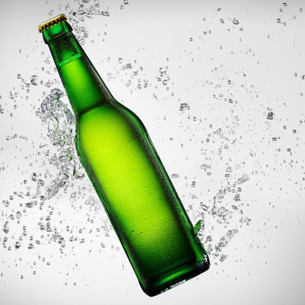Foto botella de cerveza verde cayendo en salpicaduras de agua