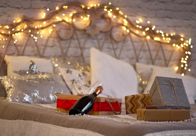 Foto botella de champagne y cajas de regalo en la cama