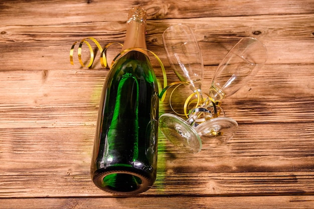 Botella de champagne y dos copas decoradas con cinta dorada sobre mesa de madera rústica