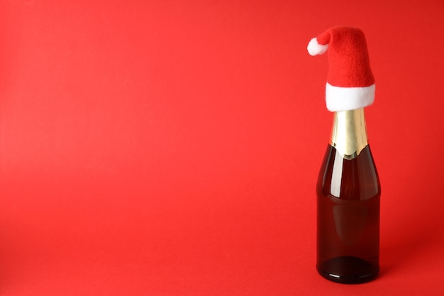 Botella de champán con gorro de Papá Noel sobre fondo rojo.