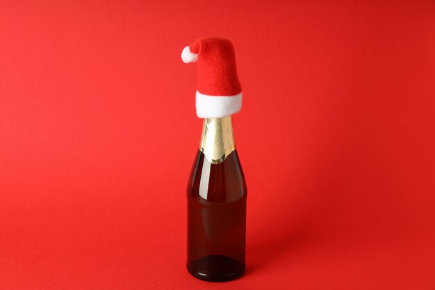 Botella de champán con gorro de Papá Noel sobre fondo rojo.