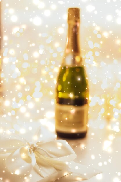 Botella de champán navideña de Nochevieja y una caja de regalo y nieve brillante sobre fondo de mármol