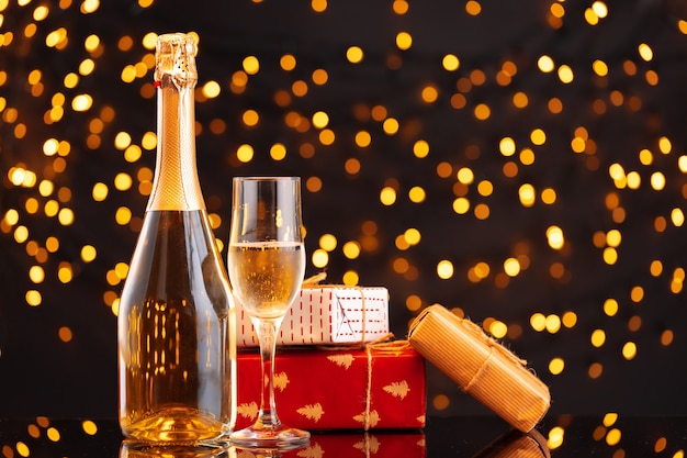 Botella de champán y regalo envuelto sobre fondo borroso de luces de Navidad vista frontal