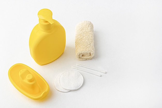 botella de champú amarilla, toalla, almohadillas de algodón y barco de juguete en blanco.