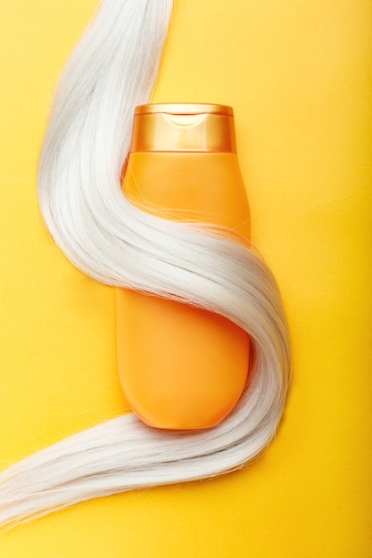 Botella de champú envuelto en un mechón de cabello rubio sobre fondo de color naranja