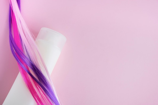 Botella de champú con muestras de cabello teñido de colores sobre fondo rosa Concepto de cuidado del cabello