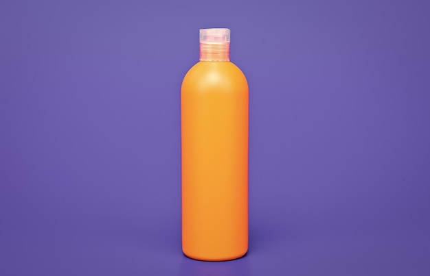 Botella de champú naranja sobre cosmetología de fondo azul