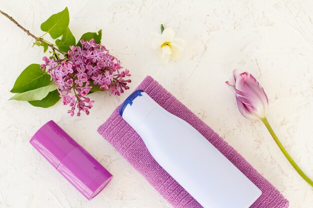 Botella de champú, toalla, desodorante, tulipán y flores lilas sobre el fondo estructurado. Cosméticos y complementos femeninos. Vista superior.