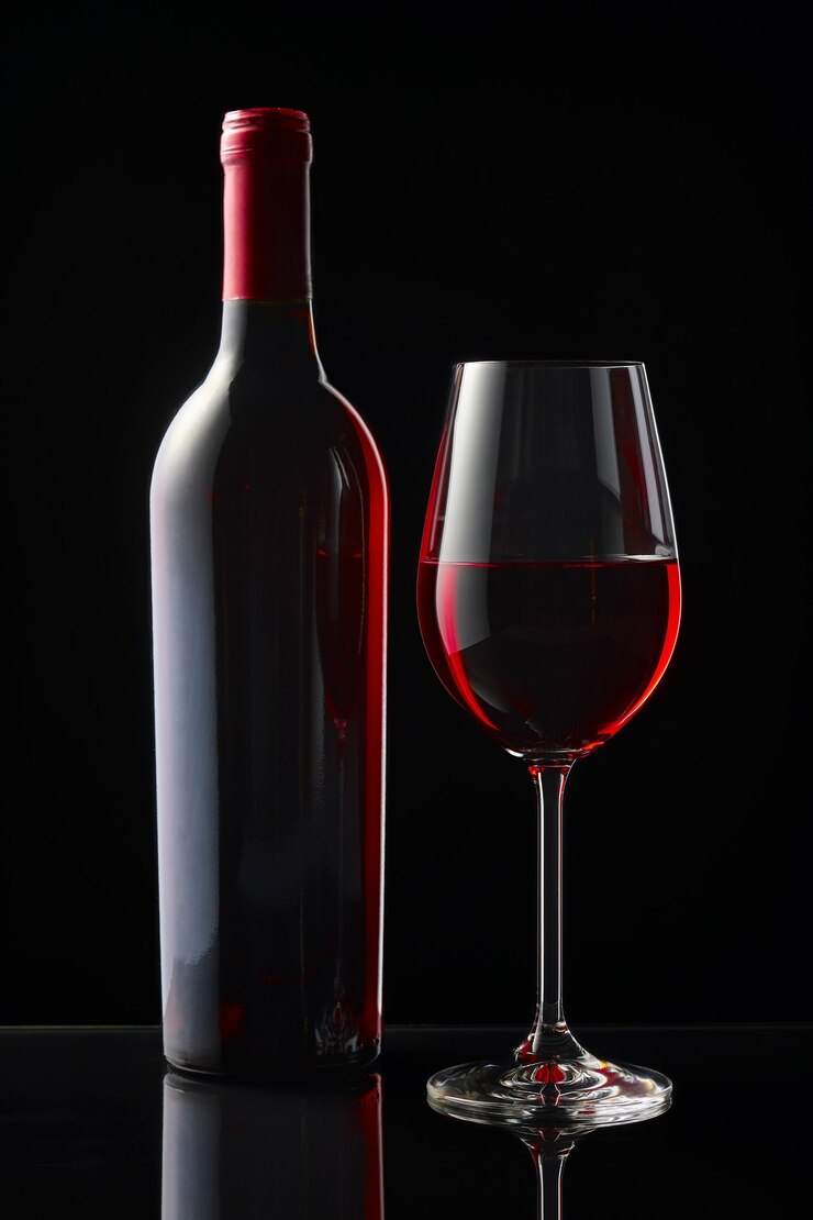 Una botella y una copa de vino tinto se colocan sobre una mesa de espejo negro.