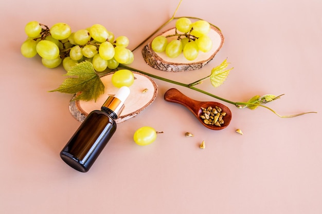 Una botella cosmética hecha de vidrio oscuro con un cuentagotas con un producto orgánico natural a base de semillas de uva se encuentra sobre una rebanada de madera con un cuidado adicional