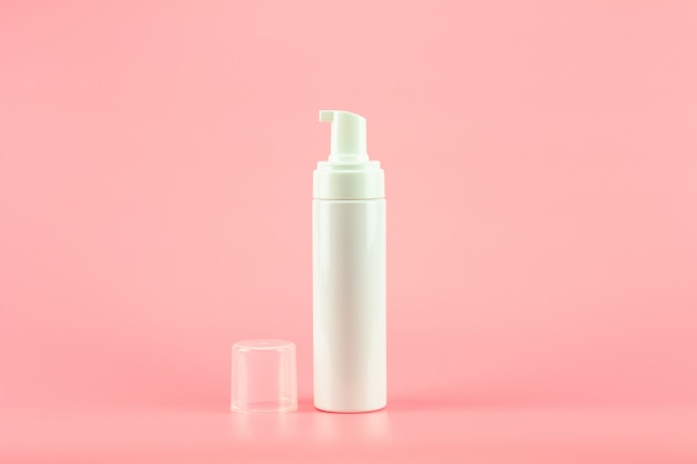 Botella cosmética plástica blanca de la loción en fondo rosado.