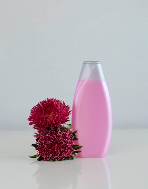 Botella cosmética vacía rosa con crema, loción hidratante o champú con hermosas flores de aster. El concepto de cosmética Spa orgánica natural desde el frente.