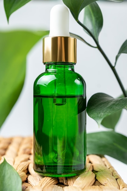 botella cosmética de vidrio verde con un gotero en un material natural beige poduim con hojas tropicales concepto de cosmética natural aceite esencial natural y productos para el cuidado de la piel