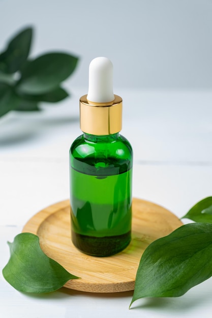 Botella cosmética de vidrio verde con un gotero sobre un fondo blanco con hojas tropicales. Concepto de cosmética natural, aceites esenciales naturales y productos para el cuidado de la piel.