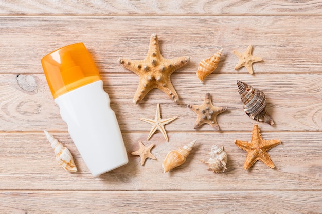 Botella de crema de protección solar y conchas marinas sobre fondo de madera. concepto plano de vacaciones de viaje de verano.