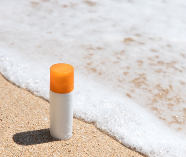 Botella de crema solar en la playa de arena junto al mar