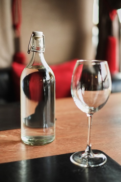 Botella de cristal alta de agua y un vaso vacío en una mesa de madera en caffe