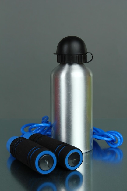 Foto botella deportiva y cuerda para saltar sobre fondo gris