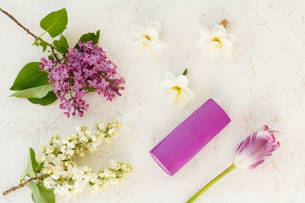 Botella con desodorante de mujer, capullos de flores de narciso, tulipán y flores lilas sobre la superficie estructurada blanca