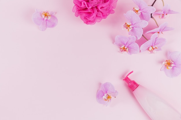 Foto botella dispensadora de plástico con jabón cosmético líquido, gel de baño o lavado íntimo, esponja violeta y flores de orquídea rosa sobre rosa claro