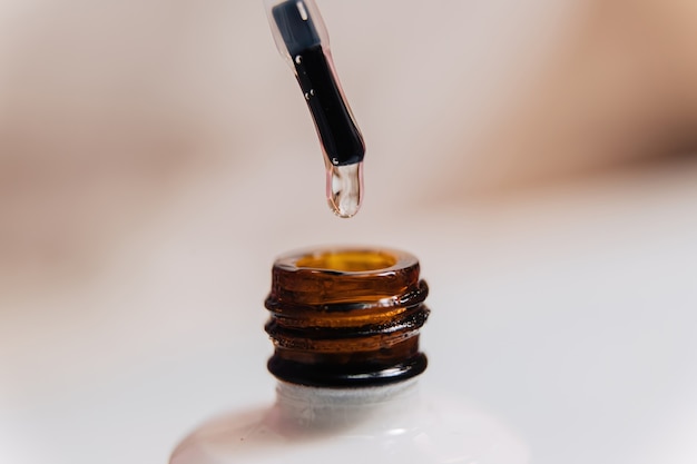 Una botella con esmalte de uñas y un cepillo con una gota de primer plano de esmalte transparente.