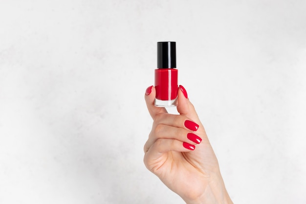 Botella de esmalte de uñas rojo en mano femenina con concepto de cuidado de piel de mano de manicura roja