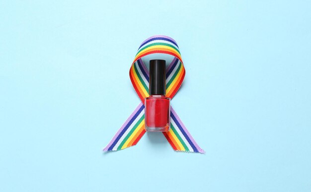 Botella de esmalte de uñas y símbolo de cinta de orgullo de cinta de arco iris LGBT sobre fondo azul Vista superior