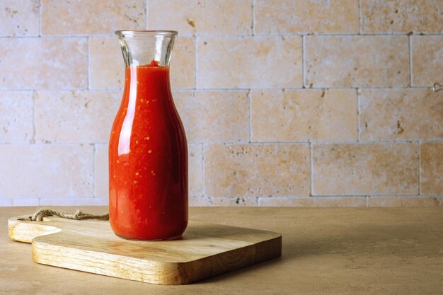 Una botella de frasco de vidrio con salsa de tomate casera se encuentra sobre una tabla de cortar de madera