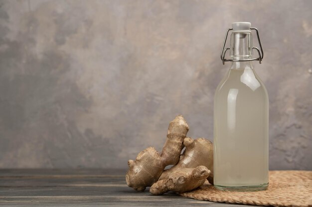 Botella con ginger ale casero limón y raíz de jengibre sobre fondo gris