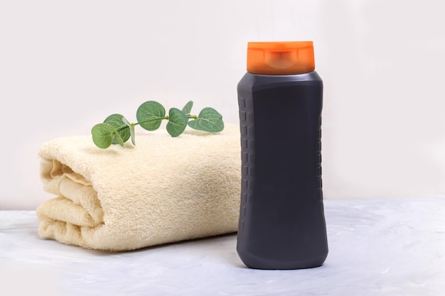 Una botella gris con gel de ducha sobre una mesa con una toalla y una rama de eucalipto