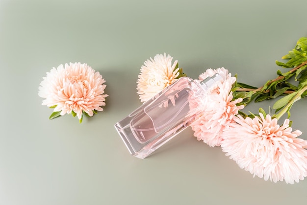 Una botella de hermoso perfume de mujer o agua de tocador se encuentra sobre flores de otoño y una presentación de fondo pastel de una fragancia sensual