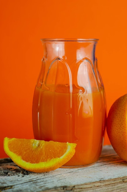 botella de jugo de naranja fresco con frutas frescas sobre una mesa de madera, fondo naranja