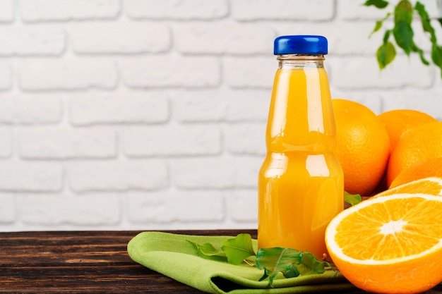 Foto botella de jugo de naranja fresco en la mesa de madera contra el fondo de pared de ladrillo blanco